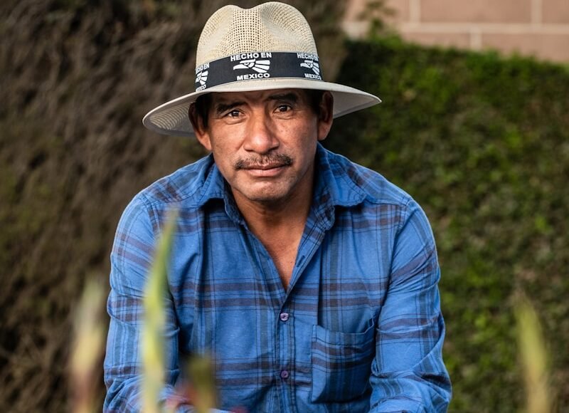 man in blue and white plaid dress shirt wearing brown cowboy hat sitting on red flower